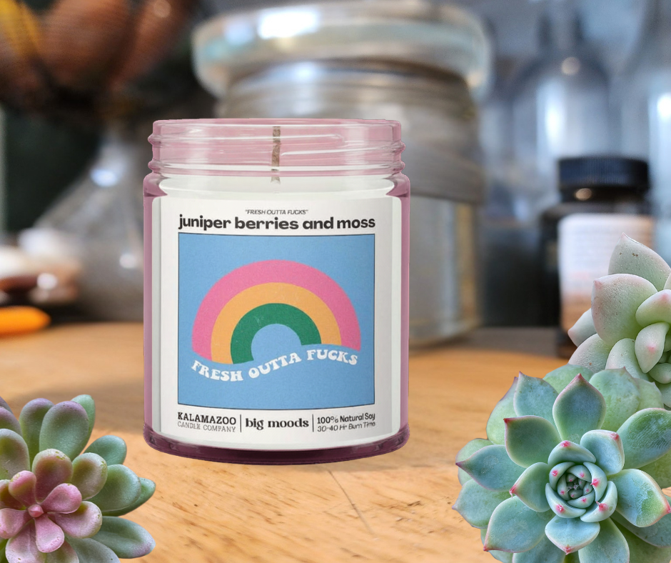 Candle jar with a colorful label featuring a rainbow on a wooden surface with succulents.
