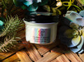 Glass jar of Tru-Nature Beauty product whipped beef tallow on a wooden surface with plants in the background