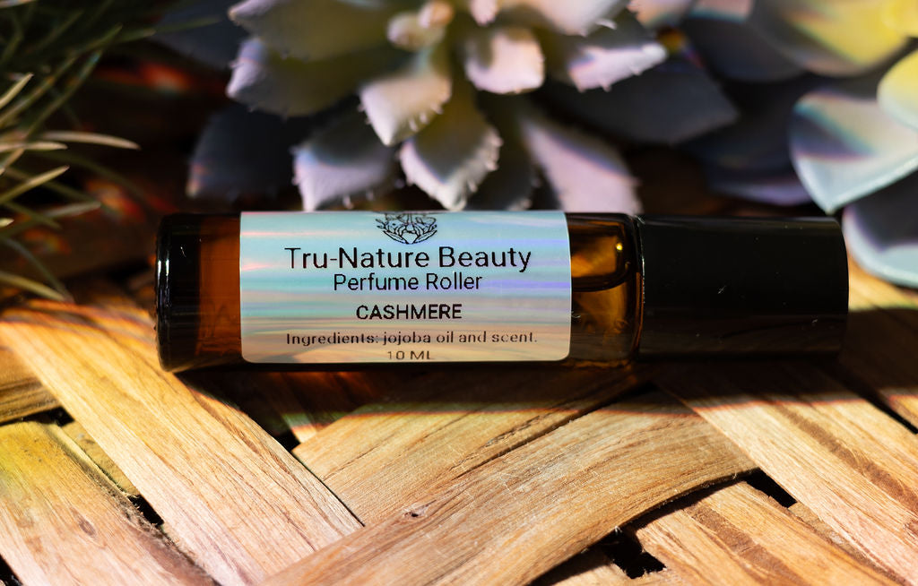 Tru-Nature Beauty perfume roller bottle labeled 'Cashmere' on a woven surface with plants in the background.