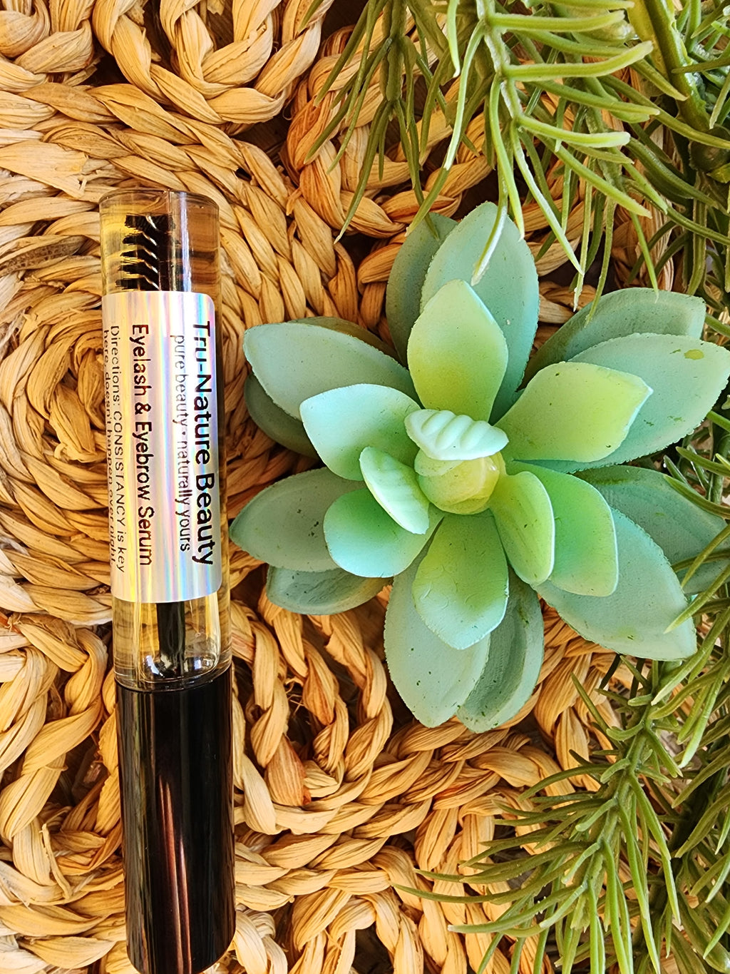 Eyebrow serum bottle on a woven surface with a succulent plant