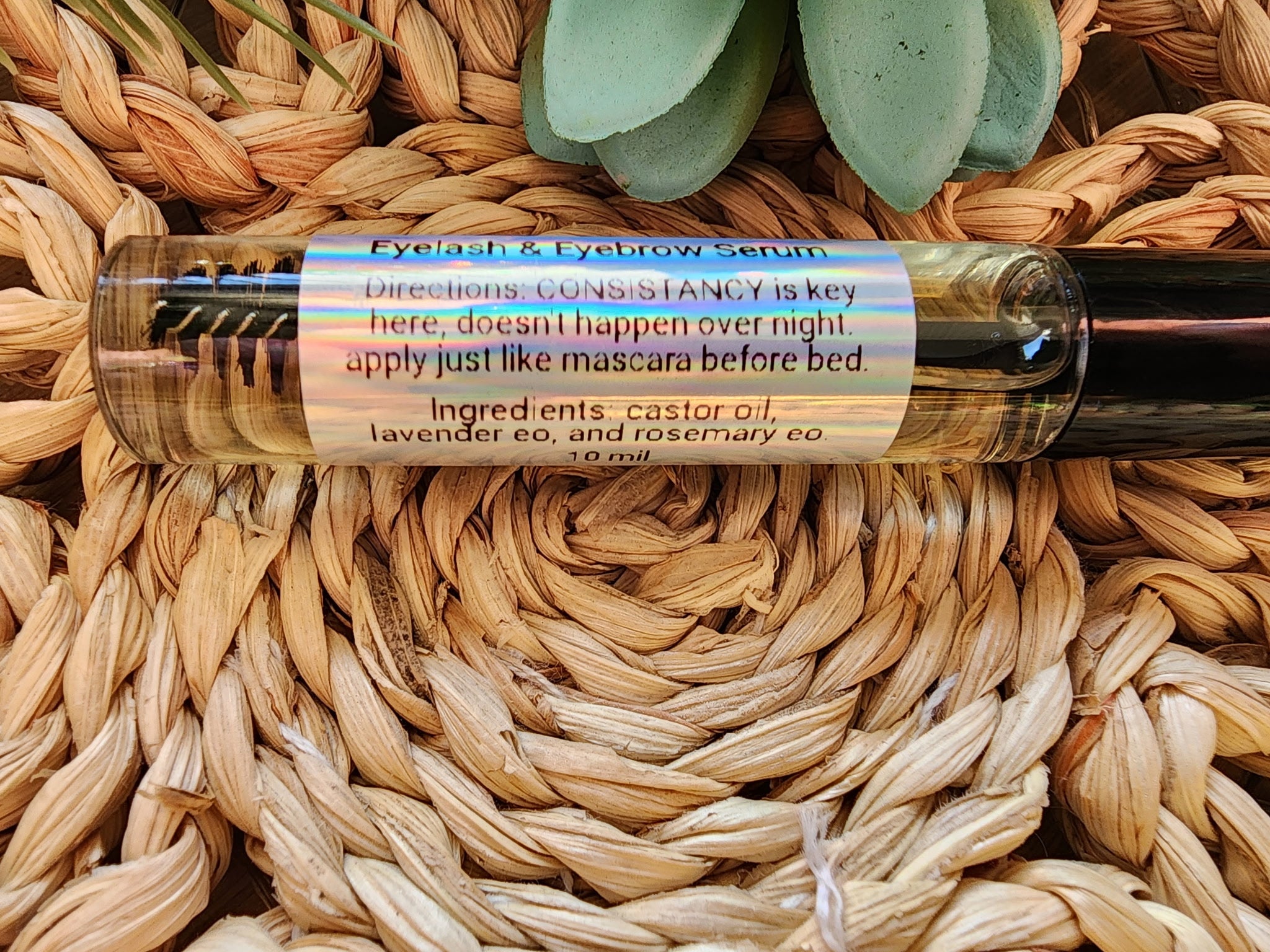 Eyelash and eyebrow serum bottle with label on a woven surface