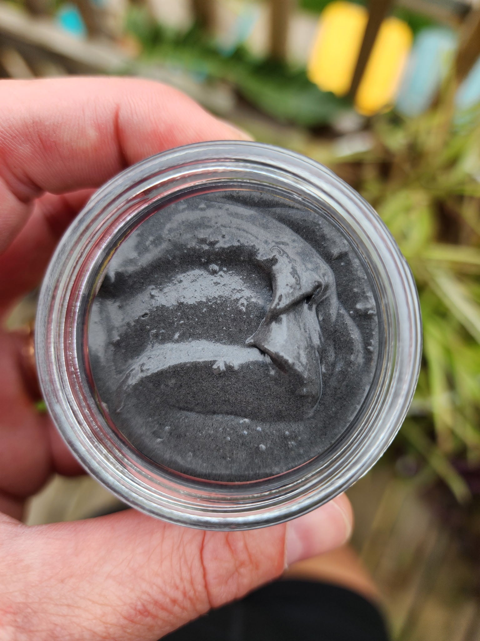 Hand holding a small jar of gray powder with a blurred natural background