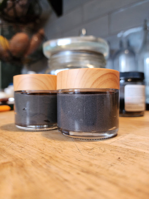 Two glass containers with wooden lids on a wooden surface, blurred background