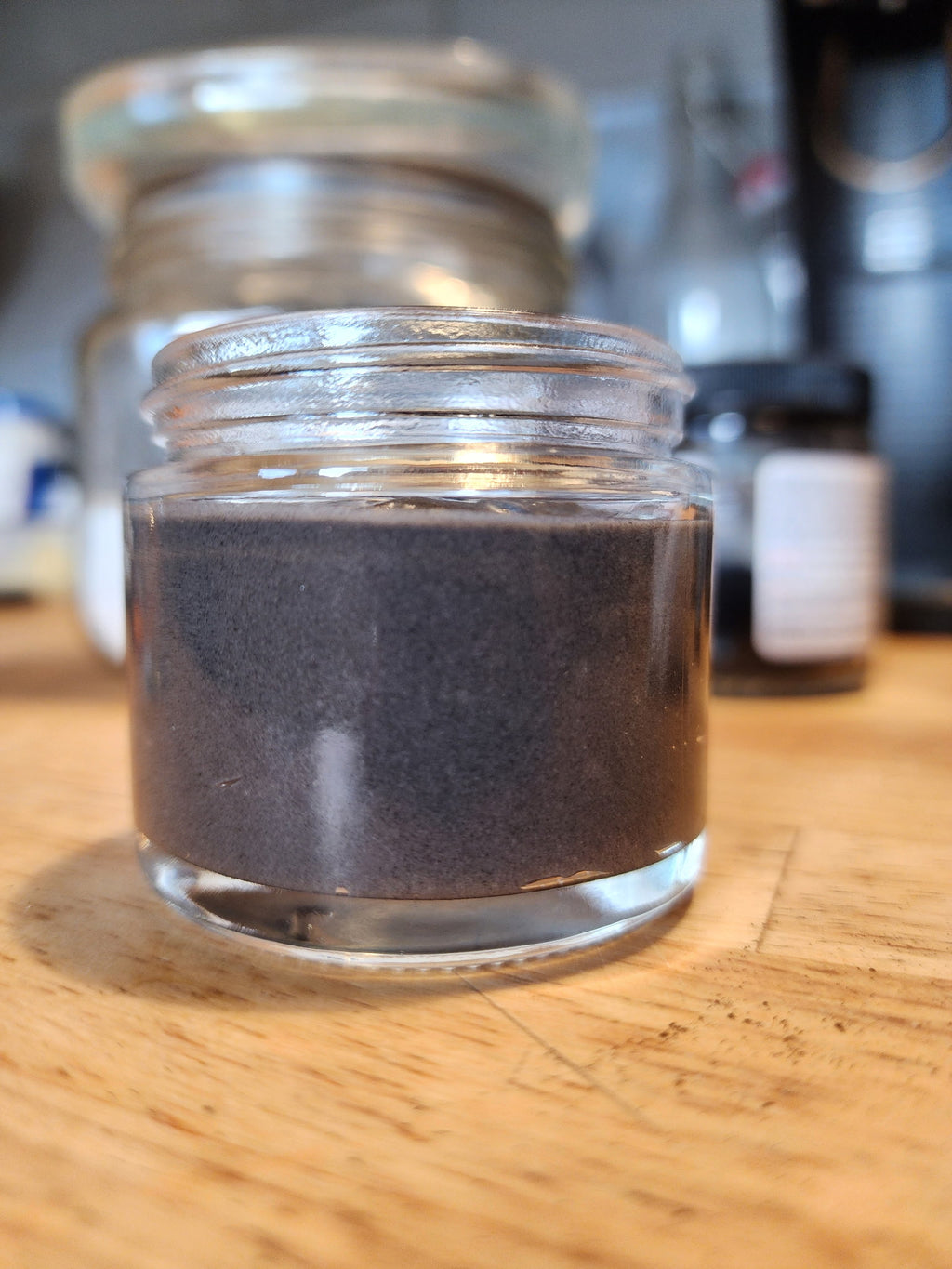 Small glass jar with dark powder on a wooden surface