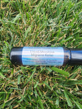 A black cylindrical roller bottle labeled 'Liquid Morphine Migraine Roller' lying on green grass.