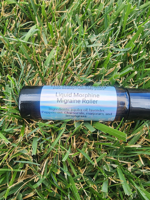 A black cylindrical roller bottle labeled 'Liquid Morphine Migraine Roller' lying on green grass.