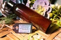 Brown bottle of Tru-Nature Beauty tanning oil on a woven surface with decorative plants.