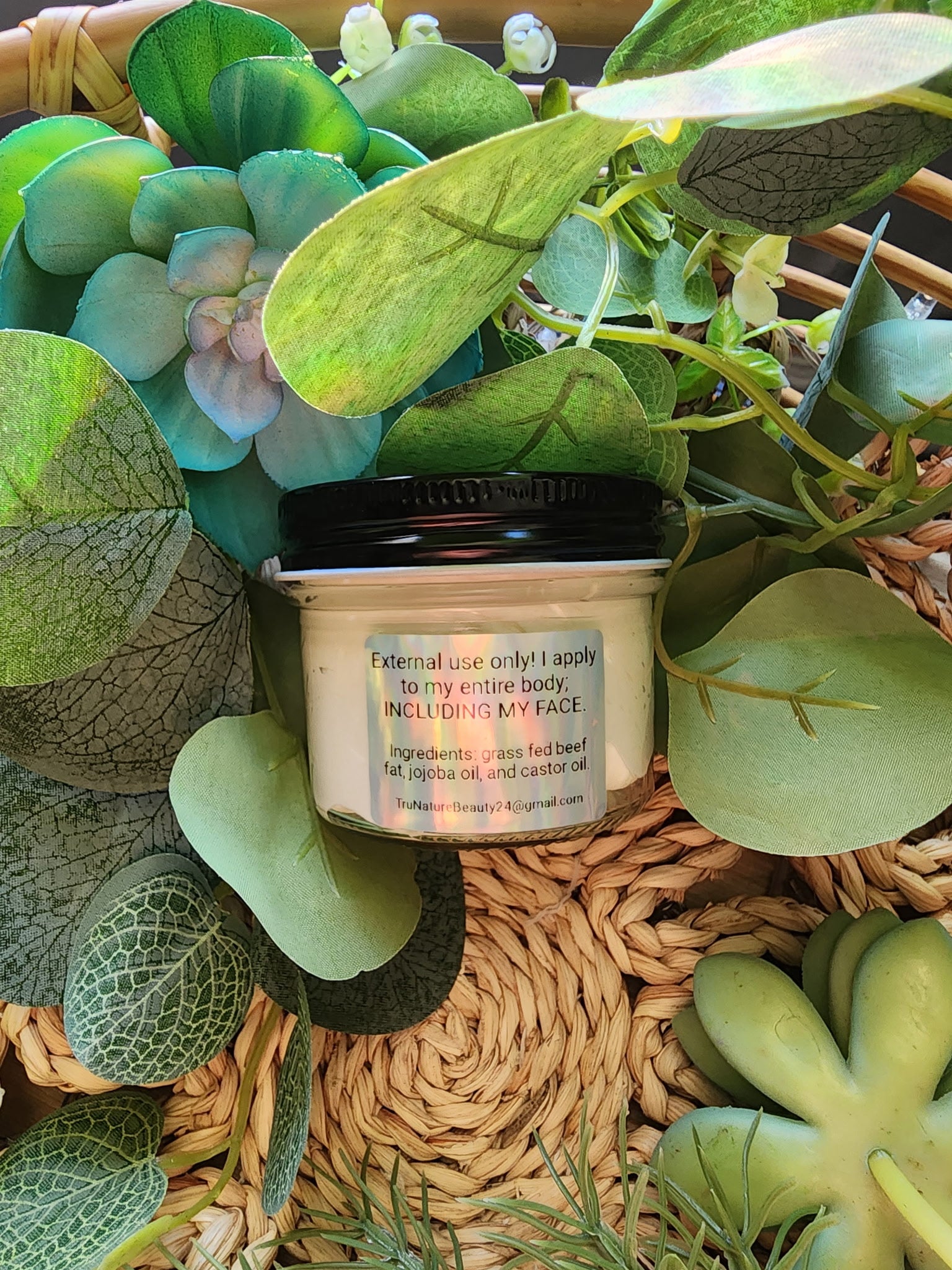 Jar of cream surrounded by green leaves on a woven surface