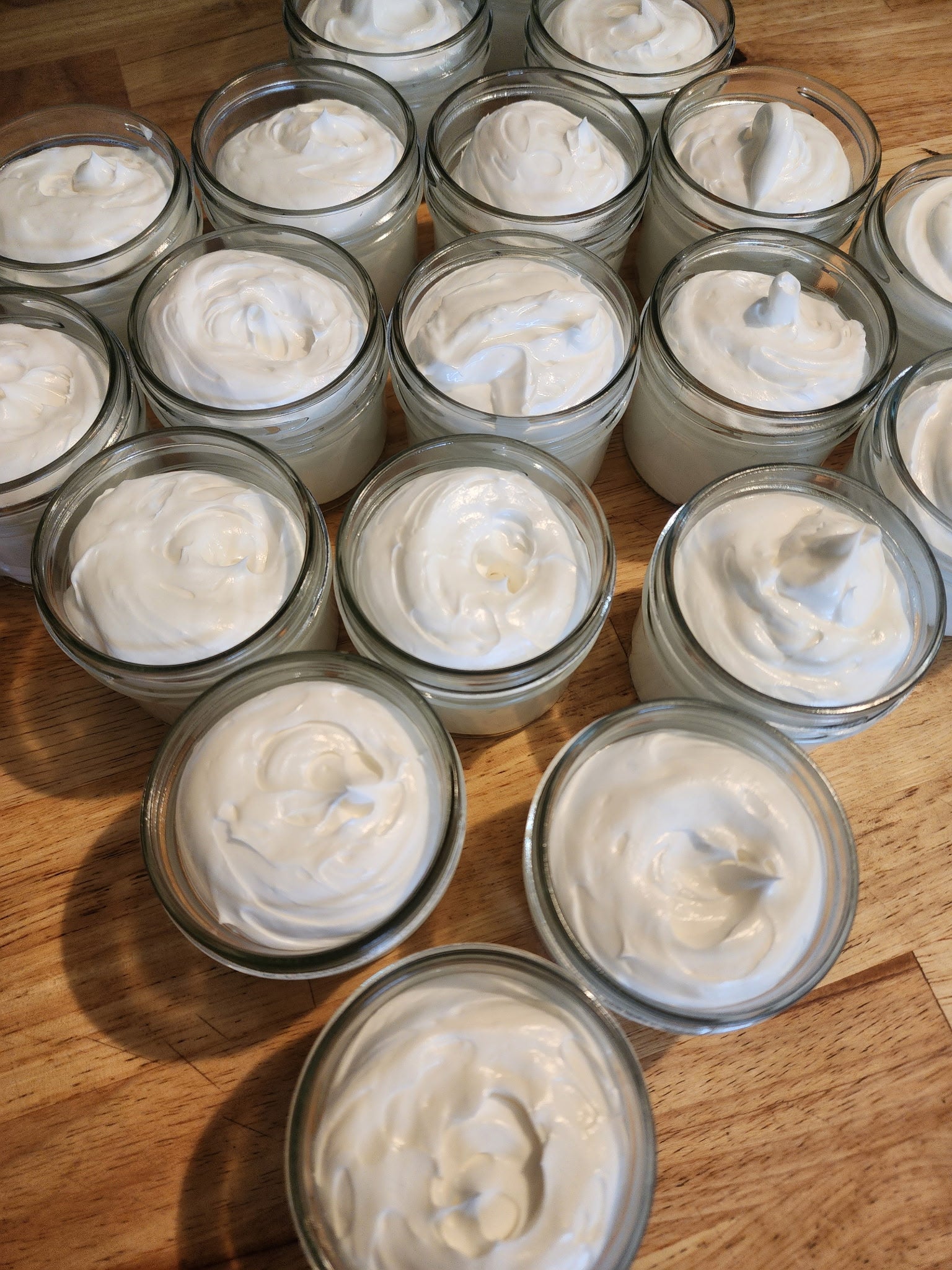 Multiple small clear glass jars filled with whipped beef tallow balm white creamy lotion arranged on a wooden surface.
